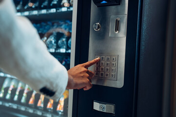 Close up view of woman's finger pushing number button on keyboard of snack vending machine....