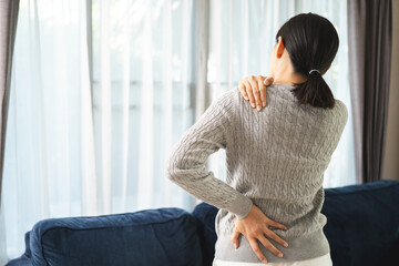 Young woman has problem with structural posture back neck and shoulder pain. Massaged her neck and shoulders for relief. reduce muscle tension on sofa couch in living room