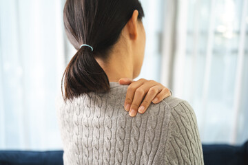 Young woman has problem with structural posture back neck and shoulder pain. Massaged her neck and shoulders for relief. reduce muscle tension on sofa couch in living room