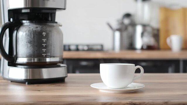 Hot cup of coffee in white modern home kitchen background. Making and pouring morning coffee at home. 