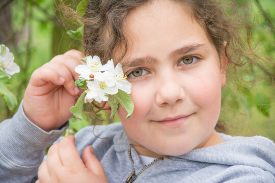 In the spring, a little girl attached to herself a flowering branch of an apple tree on which a ladybug sits.