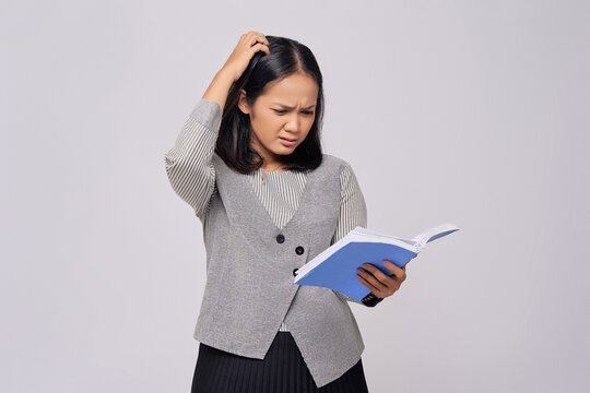 Beautiful Young Asian Woman Holding a Book of corporate business knowledge while scratching head with her hands, confused expression reading financial reports isolated on gray background