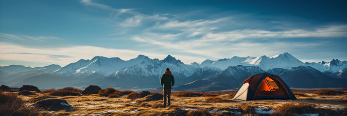 a solitary camper setting up a tent on a grassy plain, surrounded by mountain peaks capped with snow. Bright blue skies, distant silhouette of a deer, crackling bonfire nearby