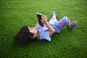 Little girl lying on the grass and playing smartphone