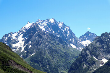 Mountain landscape: snow-capped mountains on a sunny summer day, in the foreground - mountains with vegetation