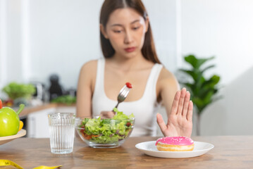 Obraz na płótnie Canvas Woman on dieting for good health concept. Close up female using hand push out her favourite donut and choose salad vegetables for good health.