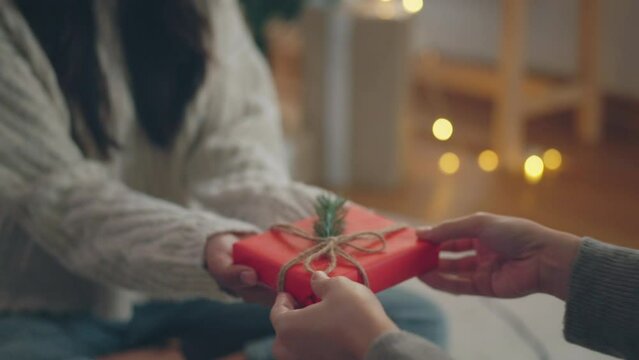 Closeup woman hands giving present gift in Christmas wrapping paper to friend. Person holding box tied with Christmas tree. Christmas, New Year, celebration.
