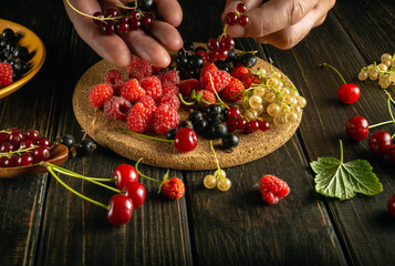 The hands of the cook sort raspberries and red currants on the kitchen table before preparing a vitamin drink. Place for prescription on dark background