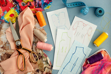 Different fabrics, accessories for sewing, drawings of patterns for making clothes. Fabrics, threads, scissors, measuring tape and pattern drawings for the sewing process.