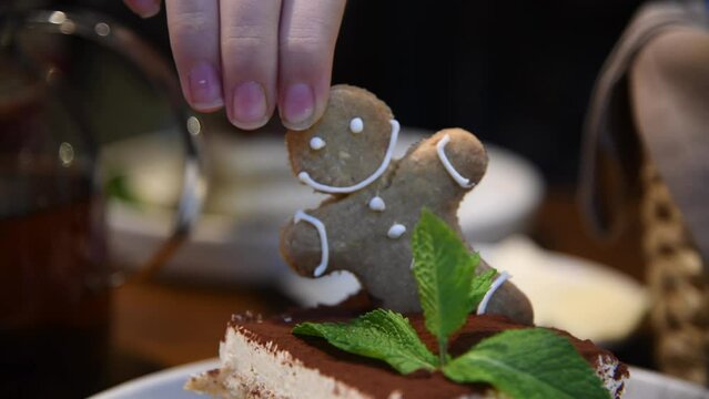 Close-up view of female hand taking out gingerbread man cookie from tiramisu cake with fresh mint in restaurant. Soft focus. Real time handheld video. Funny and cute food theme.