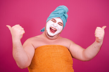 Early morning. Funny fat man enjoys life. The guy wrapped in a towel after a shower poses on a pink background. - Powered by Adobe