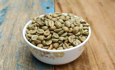 Green coffee beans in a bowl on wooden background 