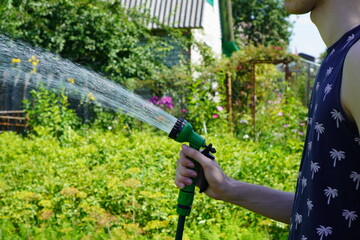 a sprayer on a hose with a jet of water in the hands of a young gardener watering beds with...