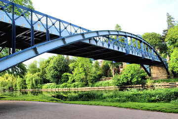 A pedestrian walking bridge across a river with lush green trees in view early in the morning