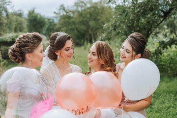 The bridesmaids look at the smiling bride. The bride and her fun friends celebrate a bachelorette party outdoors in matching dresses. The bride and friends on the grass under the open sky