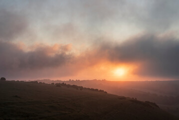 Stunning Summer sunrise from Devil's Dyke in South Downs National Park in English countryside with low lying clouds giving moody feeling