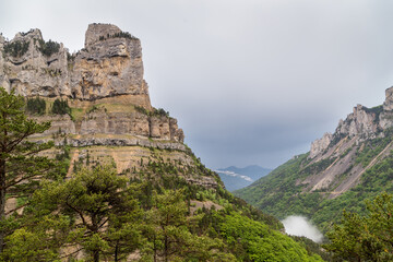 Vallée entourée de falaises abruptes calcaires sous un ciel plombé gris et menaçant. Rocher du Combeau, Châtillon en Diois