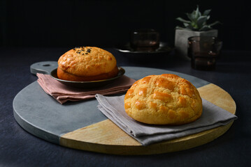 freshly handmade baked Macau crispy round polo bun bread w red bean paste on dark black luxury background with ceramic decoration halal food dessert menu for cafe