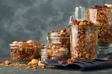 Homemade granola in glass jar with greek yogurt or milk and cashews, almonds, pumpkin with dried cranberry seeds in dark grey table background. Healthy energy breakfast or snack. Top view