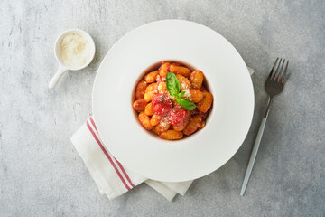 Potato gnocchi. Traditional homemade potato gnocchi with tomato sauce, basil and parmesan cheese on kitchen table on light grey kitchen table background. Traditional Italian food. Top view.