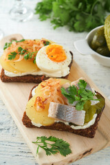 Open sandwich or smorrebrod with rye bread, herring, eggs, caramelized onions, parsley and cottage cheese on old wooden rustic table backgrounds. Danish or Scandinavian traditional food snack lunch.
