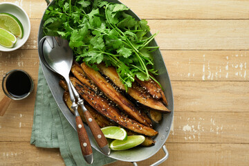 Grilled or baked eggplant slices in rice flour, with cilantro and soy sauce on old rustic wooden rustic table background. Top view with copy space.