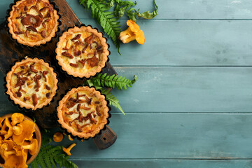 Savory hands pie with chanterelle mushrooms, cream and cheese on cutting board on rustic old wooden table background. Homemade tarts with seasonal chanterelle mushrooms. Rustic style. Top view.