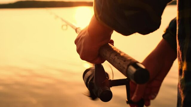 A person is fishing with a spinning rod. Fishing in the open air on a lake, river or sea at sunset with a fishing rod and reel. Stock video 4k