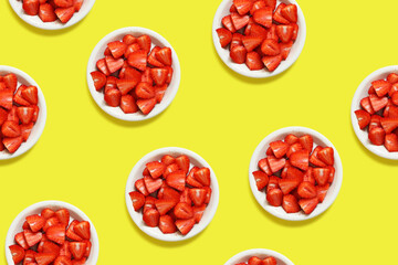 Sliced strawberries in a plate on a yellow background, top view, flat lay. Endless seamless background. Background with ripe strawberries