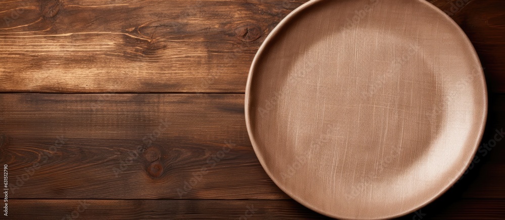 Poster brown wooden background with an empty plate and a linen napkin on top. empty space available