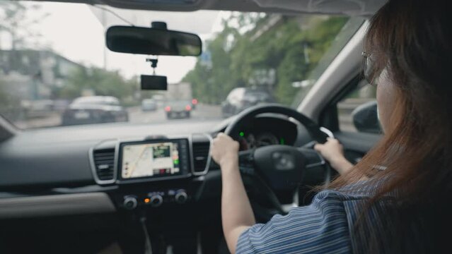 Side view of young Asian woman driving car through urban city. Women driving a car looking GPS map on screen in the car