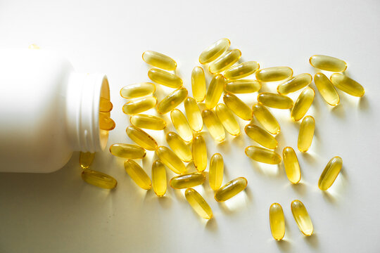 Open bottle with omega-3 capsules. Next to the lid with capsules. Medical concept. Pile of yellow softgel capsules Omega 3 fish oil scuttered from a white bottle bottle. Health care concept.