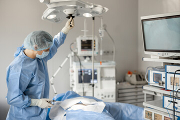 Surgeon sets up a light, preparing for invasive procedure at operation room. Surgical treatment concept