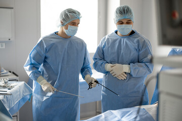 Two surgeons in uniform stand with endscopes preparing for minamal invasive procedure for a patient...