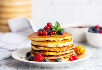 Healthy summer breakfast, homemade classic american pancakes with fresh fruit and honey, morning light gray stone background copy space top view