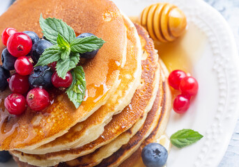 Healthy summer breakfast, homemade classic american pancakes with fresh fruit and honey, morning light gray stone background copy space top view