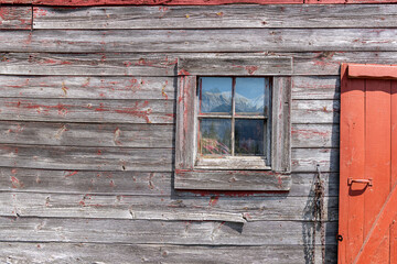 Fototapeta na wymiar Wooden barn exterior with mountains reflected in window.