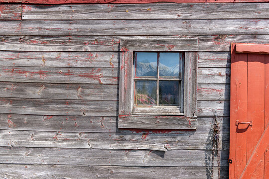 Wooden barn exterior with mountains reflected in window.
