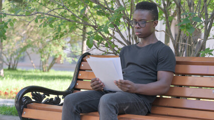 Obraz premium Young African Man Reading Documents while Sitting Outdoor