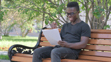 Young African Man Celebrating while Reading Documents Outdoor