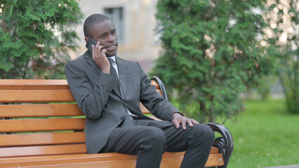 Fototapeta premium African Businessman Talking on phone while Sitting Outdoor on a Bench