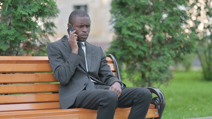 Obraz premium Upset African Businessman Arguing on phone while Sitting Outdoor on a Bench
