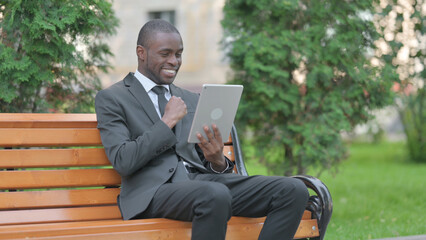 African Businessman Celebrating Success on Tablet while Sitting Outdoor on a Bench