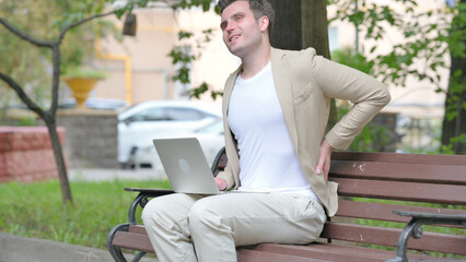 Fototapeta premium Casual Young Man Using Laptop with Back Pain while Sitting Outdoor