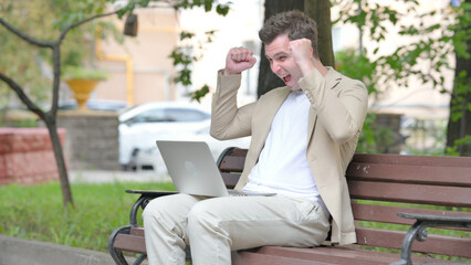 Fototapeta premium Excited Casual Young Man Celebrating Success on Laptop Outdoor