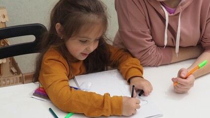 Little girl taking online art class with mother helping her at home. Child and parent drawing...