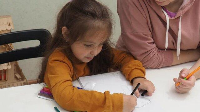Little girl taking online art class with mother helping her at home. Child and parent drawing together to video tutorial. Mom and daughter do homework, creativity together. maternal care