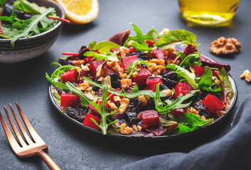Vegan salad with beet, dried plums, arugula, swiss chard and walnuts, black stone table background....