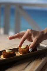 Female hand stretches out in front of a tranquil seascape, reaching for a small appetizer