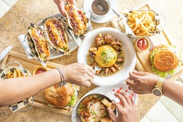 Top view of the hands of people grabbing food from the table served with hamburger, tacos